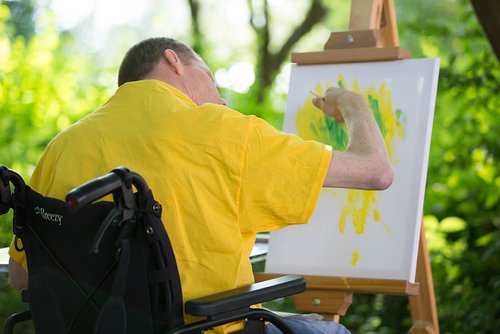 Ein Mann im Rollstuhl malt ein Bild an einer Staffelei.