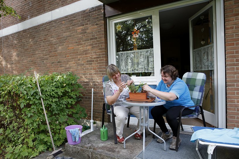 Zwei Frauen kümmern sich auf der Terrasse um einen Blumenkasten.