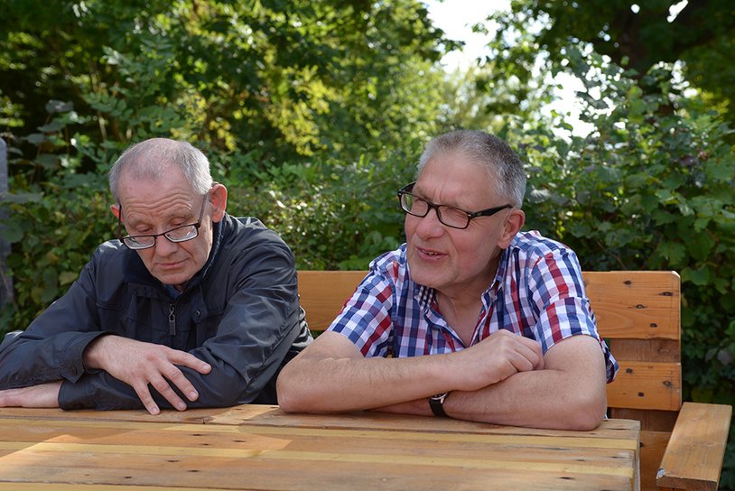 Zwei Männer sitzen auf einer Bank im Garten.