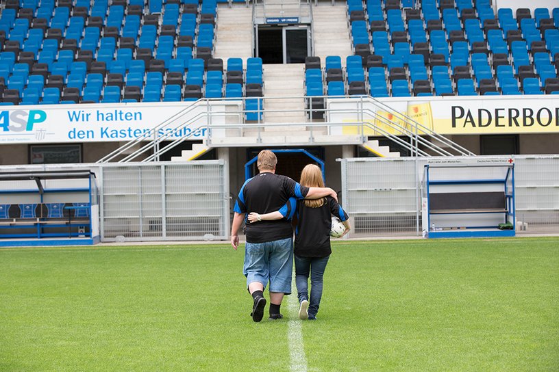 Ein Paar verlässt Arm in Arm den Rasen eines Fussballstadions.